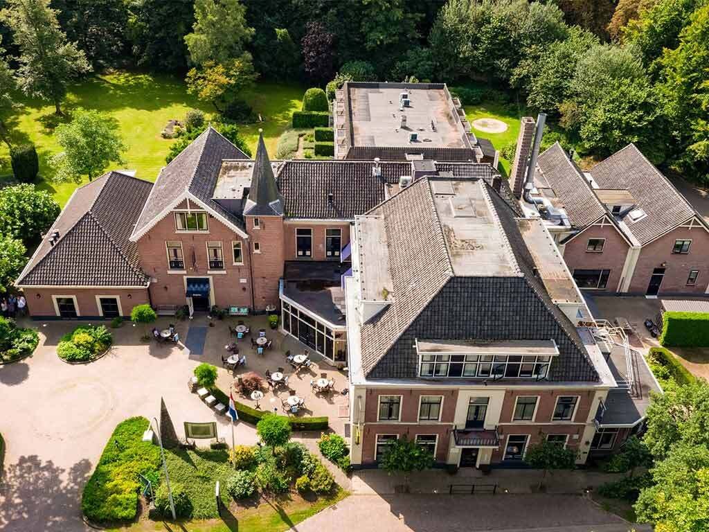Un grand bâtiment historique doté de plusieurs ailes, d’une cour centrale et d’un jardin bien entretenu.