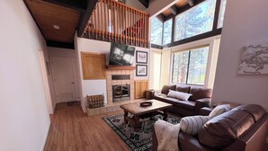 A living room with a fireplace, a sofa, a coffee table, and a TV mounted on the wall. - Cascade Hideaway in Lake Village With Private Hot Tub! (Stateline)