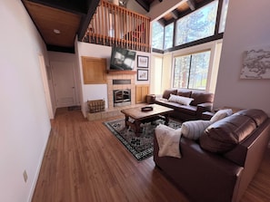A living room with a fireplace, a sofa, a coffee table, and a TV mounted on the wall.