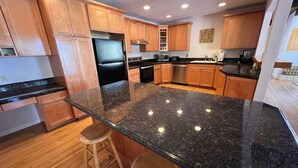A modern kitchen with wooden cabinets, a black granite countertop, stainless steel appliances, and a bar stool. - Cascade Hideaway in Lake Village With Private Hot Tub! (Stateline)