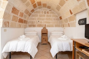 A room with two beds, a wooden nightstand, a television, and a stone arch ceiling. - Casa Tino 2 – Elegant Stone Retreat with Rooftop Terrace (Polignano a Mare)