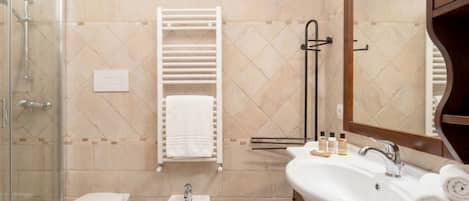 A bathroom with a shower, bidet, sink, and towel rack.