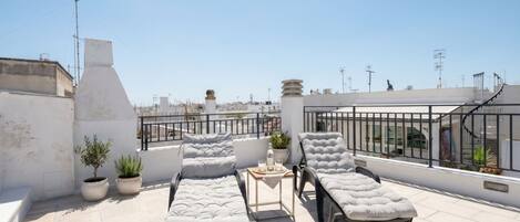 Terraza en la azotea con dos sillones, una mesita y plantas en macetas.