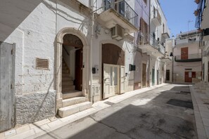 A narrow street with buildings featuring arched doorways, a staircase, and balconies. - Casa Tino 2 – Elegant Stone Retreat with Rooftop Terrace (Polignano a Mare)