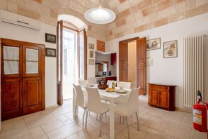 A dining area with a white table, chairs, and a kitchen in the background. - Casa Tino 2 – Elegant Stone Retreat with Rooftop Terrace (Polignano a Mare)