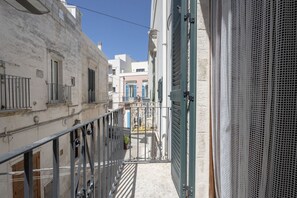 A narrow street with buildings on either side, a metal gate, and a balcony with a metal railing. - Casa Tino 2 – Elegant Stone Retreat with Rooftop Terrace (Polignano a Mare)