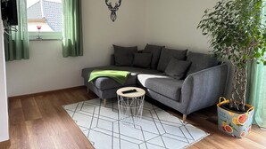 Un soggiorno con un divano grigio, un tavolino rotondo, una pianta in vaso e una decorazione a forma di cervo appesa al muro.