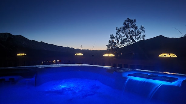 Ein Bereich mit Whirlpool und Wasserfall, umgeben von Bergen und beleuchtet mit warmem Licht.