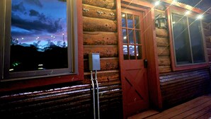 Eine Blockhütte mit einem großen Fenster, einer Tür mit Glasfeldern und Lichterketten entlang des Daches.