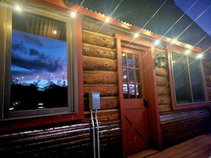 A log cabin with a large window, a door, and string lights.