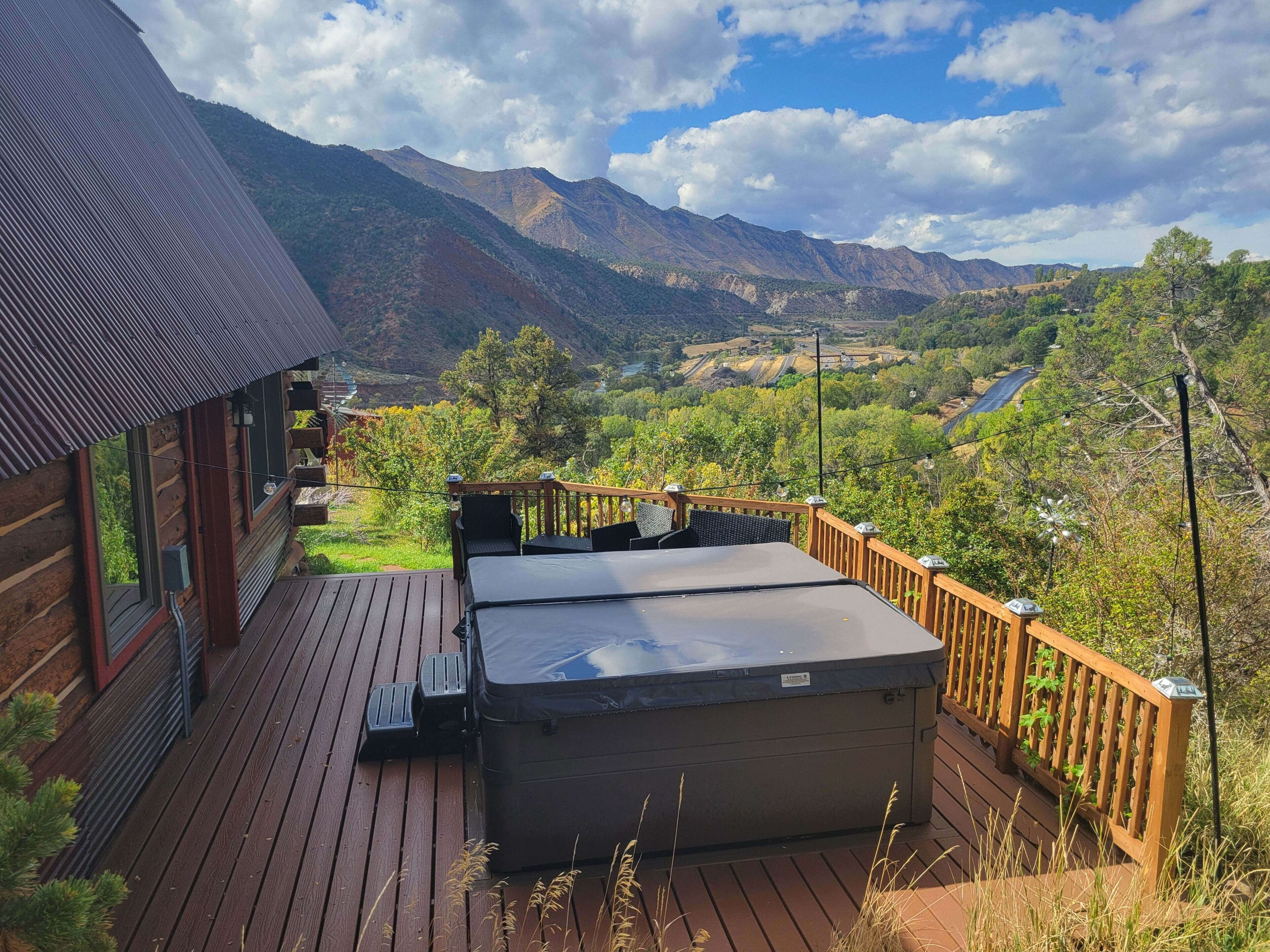 Una terrazza in legno con vasca idromassaggio, con vista su un paesaggio montuoso.