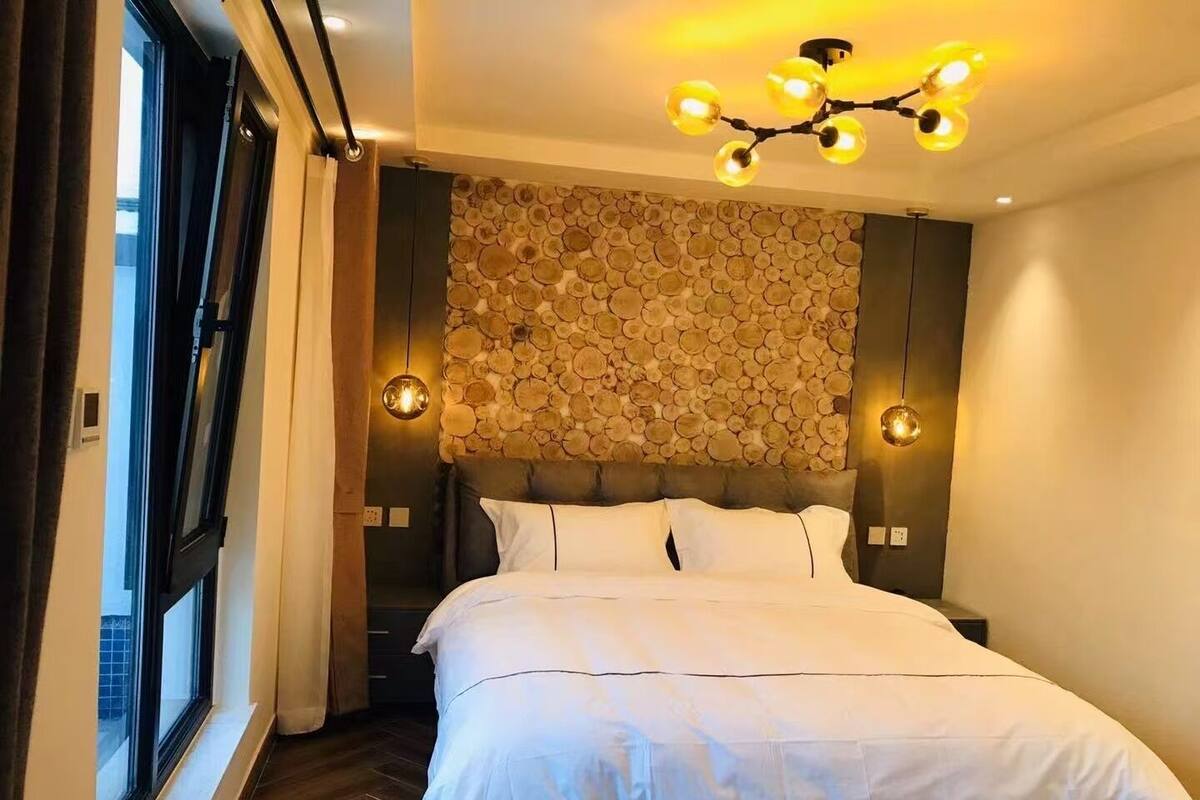 A bedroom with a stone wall headboard, a large bed with white bedding, and a modern chandelier.