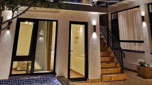 A modern house with a glass balcony, a wooden staircase, and a pool area.