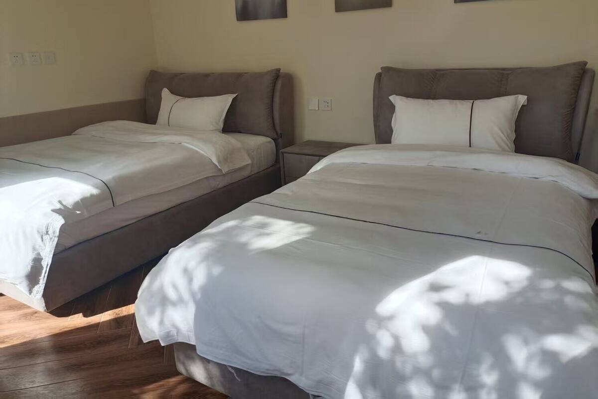 A room with two beds, a nightstand, and a wall-mounted power outlet.