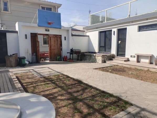 A courtyard with a basketball hoop, a wooden door, a red vehicle, and a fire extinguisher.