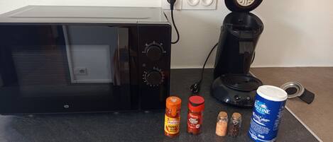 Una cocina con microondas, cafetera y diversos condimentos sobre la encimera.