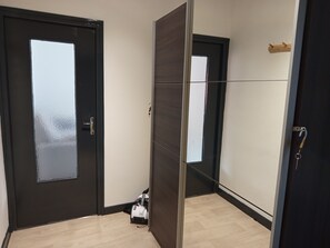 Ein Zimmer mit einer dunklen Tür, einem Spiegel, einer kleinen Tasche auf dem Boden und einem Holzboden.