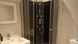 Et moderne badeværelse med et glasafskærmet brusebad, en hvid vask og et toilet.