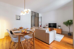 Ein modernes Wohnzimmer mit Esstisch, Sofa, Fernseher und einer Zimmerpflanze.