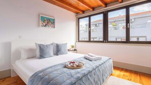 Une chambre à coucher avec un lit, une fenêtre avec des stores, un tableau accroché au mur et un plateau avec de la nourriture posé sur le lit.