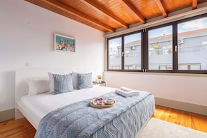 Ein Schlafzimmer mit Bett, einem Fenster mit Jalousien, einem Bild an der Wand und einem Tablett mit Essen auf dem Bett.