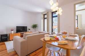 Ein modernes Wohnzimmer mit Sofa, Fernseher, Esstisch gedeckt für ein Frühstück und einem großen Fenster.