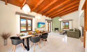 A spacious dining area with a wooden table and chairs, a television mounted on the wall, and a view of the outdoors through large windows. - Vegghera Villa Private Pool (Kavros)