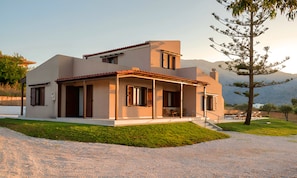 A modern two-story house with a covered patio, a small front yard, and a mountainous backdrop. - Vegghera Villa Private Pool (Kavros)