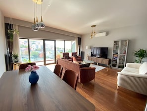 Una sala de estar moderna con comedor, un conjunto de sofás, televisión y un ventanal con vista a la ciudad.