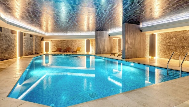 An indoor swimming pool with a clear blue water surface, surrounded by walls with a textured stone finish, and a ceiling with a cloud-like pattern. - Benesta Centro by GOLDFINCH (Istanbul)