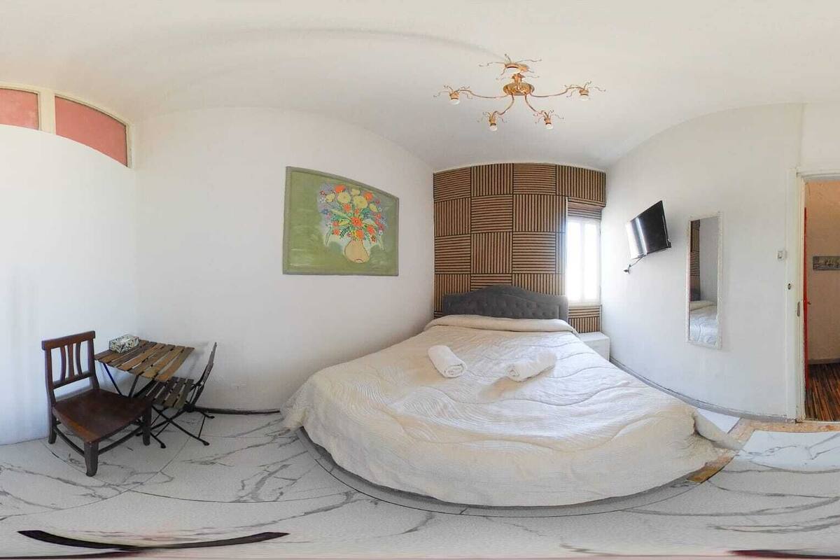Un dormitorio con cama, una silla, un cuadro, televisor y pared con diseño.