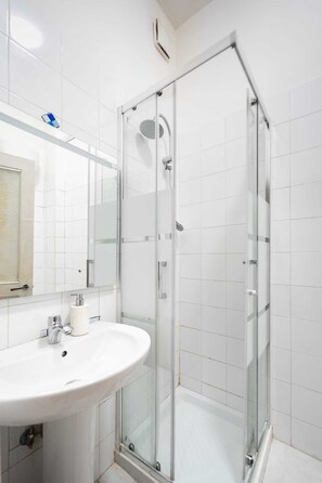 A bathroom with a glass-enclosed shower, a white sink, and a mirror above the sink. - Tangueu Suites & Rooms (Naples)
