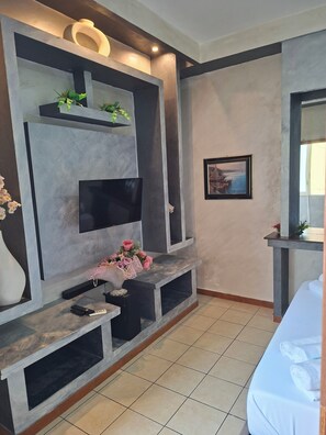 A modern living room with a flat-screen TV, built-in shelves, a console table with a vase and flowers, and a framed picture on the wall. - Tangueu Suites & Rooms (Naples)