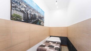 Pieni, kapea hotellihuone, jossa on sänky, suuri ikkuna ja näkymä kaupunkiin.