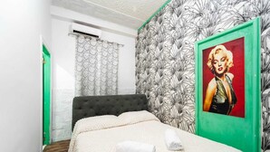 Hotellihuone, jossa on sänky, vihreäkehysinen taulu, kuviollinen verho ja vihreä ovi.