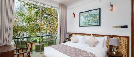 A hotel room with a large bed, a ceiling fan, a balcony with chairs, and a painting on the wall.