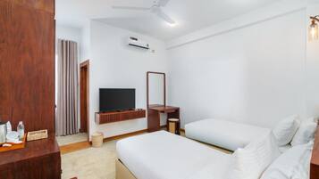 A hotel room with a bed, a TV, a ceiling fan, an air conditioning unit, and a wooden desk with a mirror.