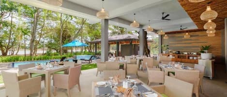 An outdoor dining area with wicker furniture, ceiling fans, and hanging lights.