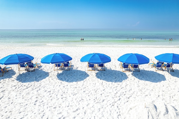 A beach with five blue umbrellas and matching lounge chairs arranged in a row. - New Luxurious 1 BR/2 Ba with 2 Kings and a Queen w/ Free Beach Service for 4! (Fort Walton Beach)
