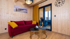 Um quarto com painéis de madeira, um sofá vermelho, uma mesa redonda e um relógio na parede.