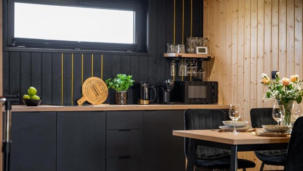 Uma cozinha moderna com armários pretos, bancada de madeira e um espaço de refeições com mesa posta para dois.