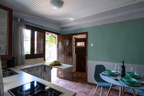 A kitchen with a built-in stove, a dining area with a table set for two, and a door leading to a room. - Sweet Home Country House with Private Terrace, Wi-Fi, and Air Conditioning (Volos)