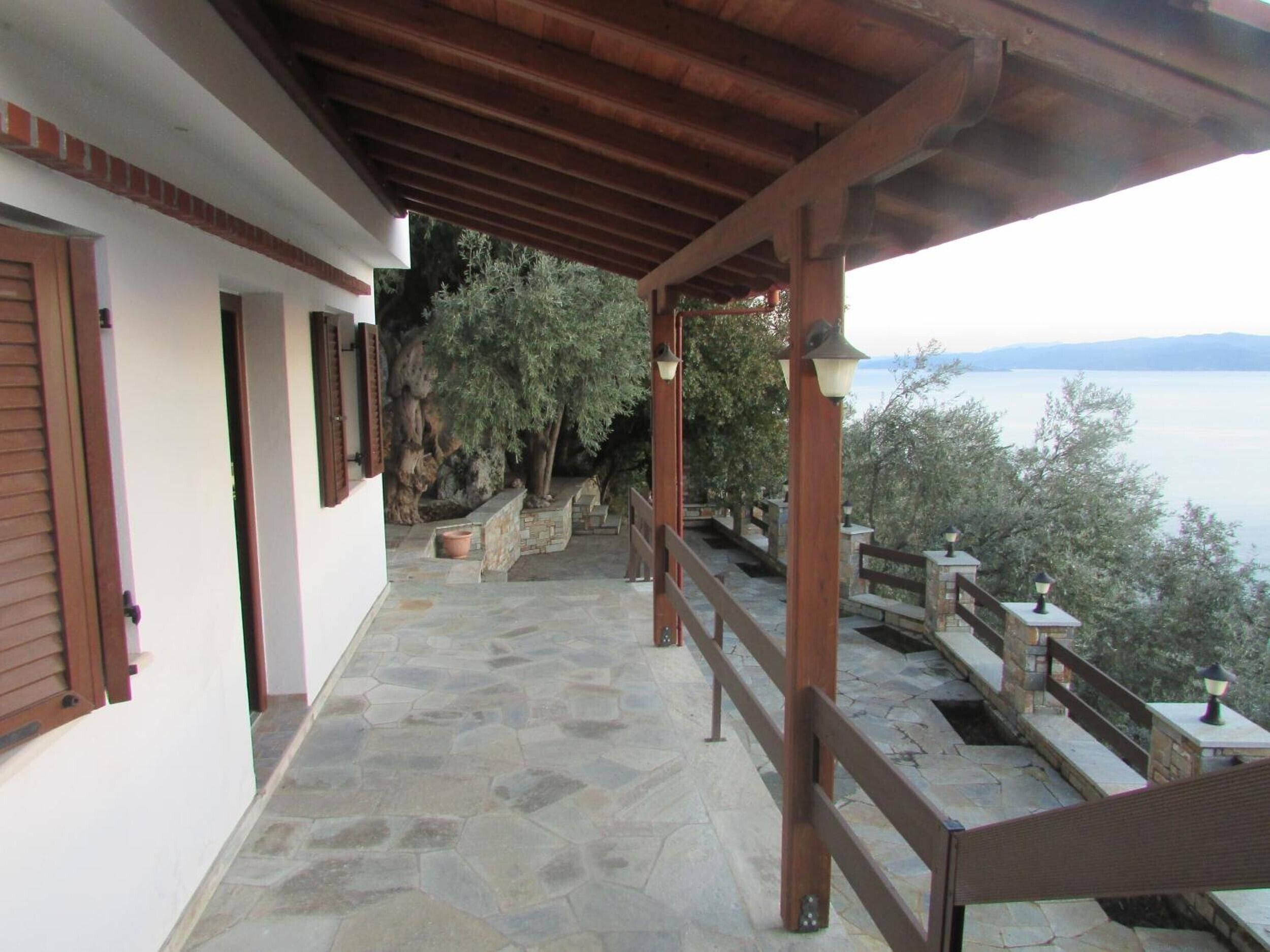 Un balcone con pavimento in pietra, ringhiere in legno, vista sul mare e un muro di pietra con una pianta in vaso.
