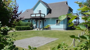 Une maison avec un grand jardin devant, un balcon et un ciel dégagé.
