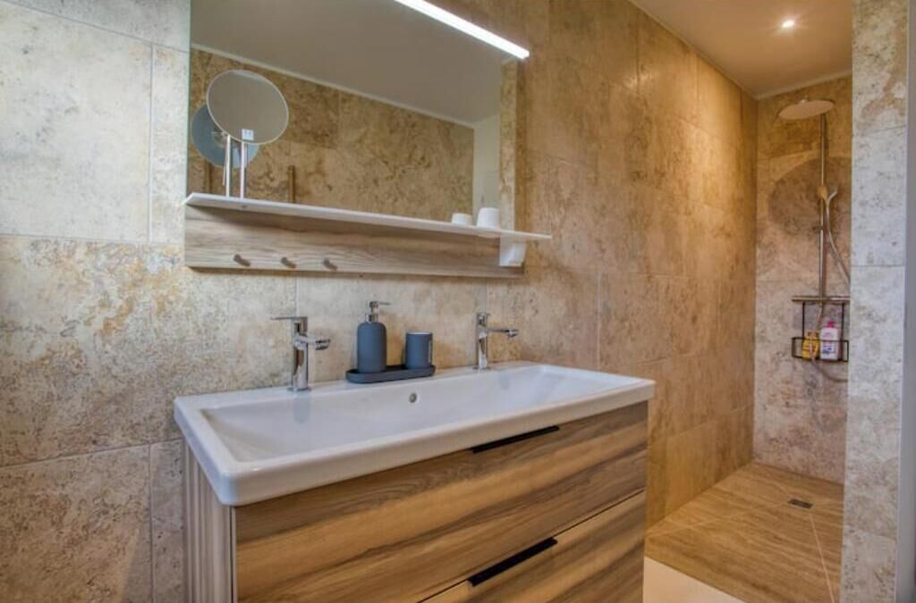 Un baño moderno con un lavamanos grande, tocador de madera, un espejo y una zona de ducha.