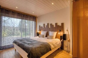 Een slaapkamer met een groot bed, een raam met dunne gordijnen, een wandlamp en een girafbeeld.