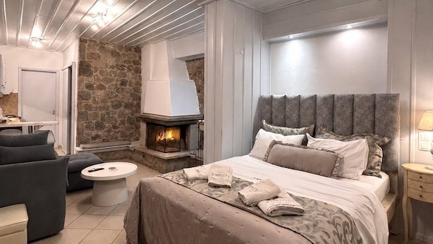 Una camera da letto moderna con camino in pietra, un letto grande con molti cuscini, un divano e un tavolino rotondo.