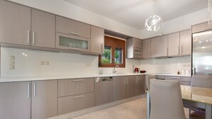 Cozinha moderna com eletrodomésticos de aço inoxidável, uma janela e um espaço de refeições com uma cadeira.