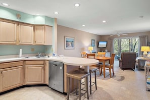 A kitchen with wooden cabinets, a dishwasher, a dining area with a table and chairs, and a ceiling fan. - Eagle Way 2  Access to Pools (Rehoboth Beach)