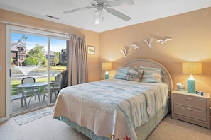 A bedroom with a bed, two bedside tables, a ceiling fan, a sliding glass door to the outside, and a view of the outside. - Eagle Way 2  Access to Pools (Rehoboth Beach)